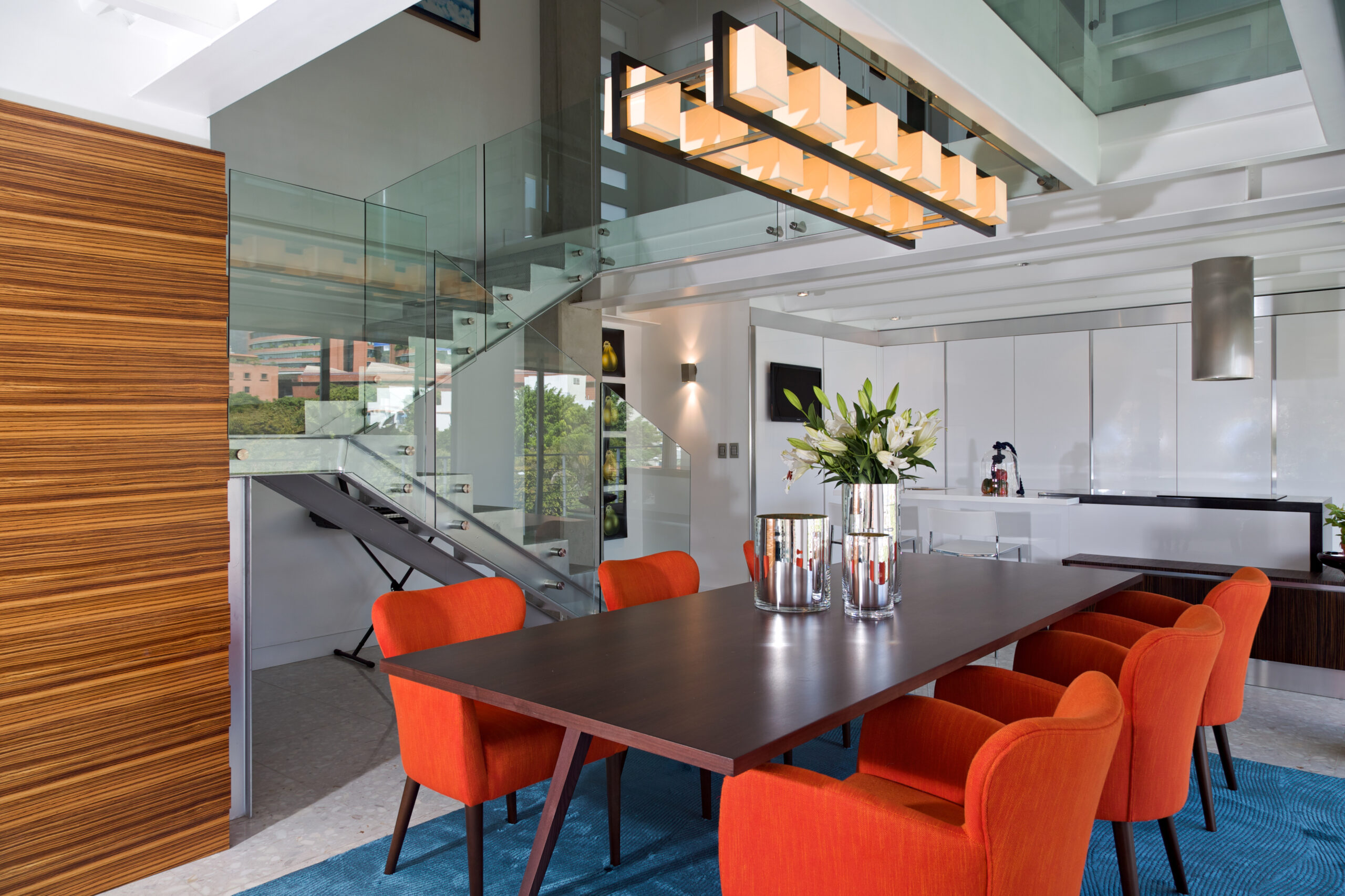 Modern and bright dining room of luxurious apartment. Interior design and decoration, dark wood table and orange chairs on blue carpet.